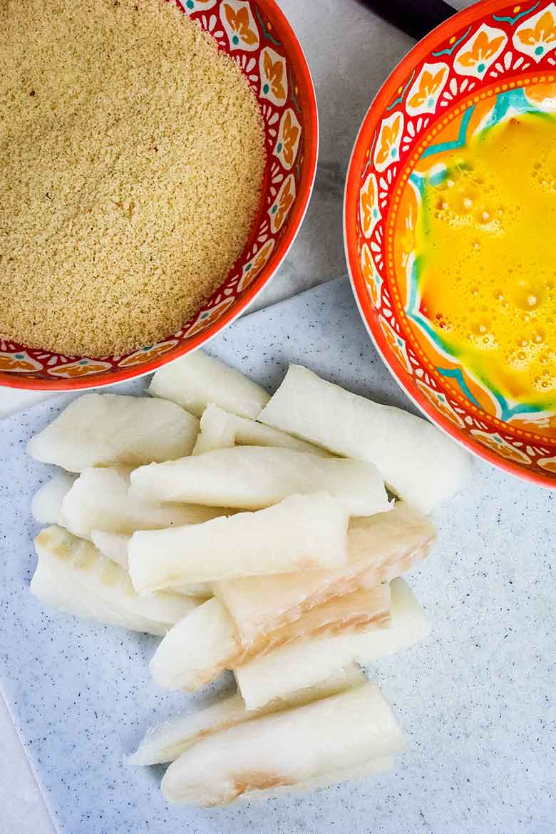 Cod Fish cut into 1x2 sticks with a bowl of egg wash and bowl of almond flour coating.