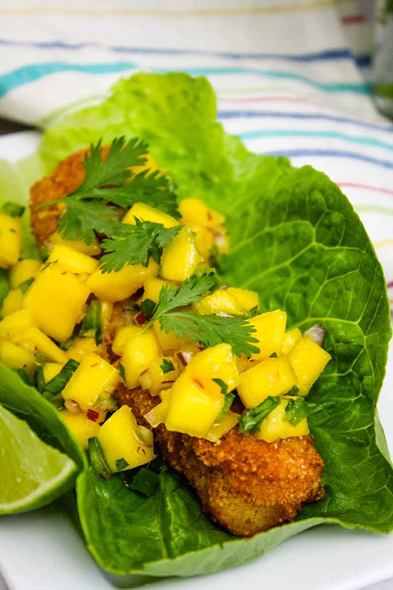 A Fried Fish Taco topped with Spicy Mango Salsa in a lettuce cup.