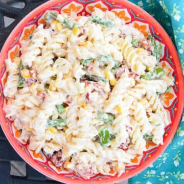 An orange and blue patterned bowl with spiral pasta mixed in a creamy dressing with asparagus, corn, and sun dried tomatoes.