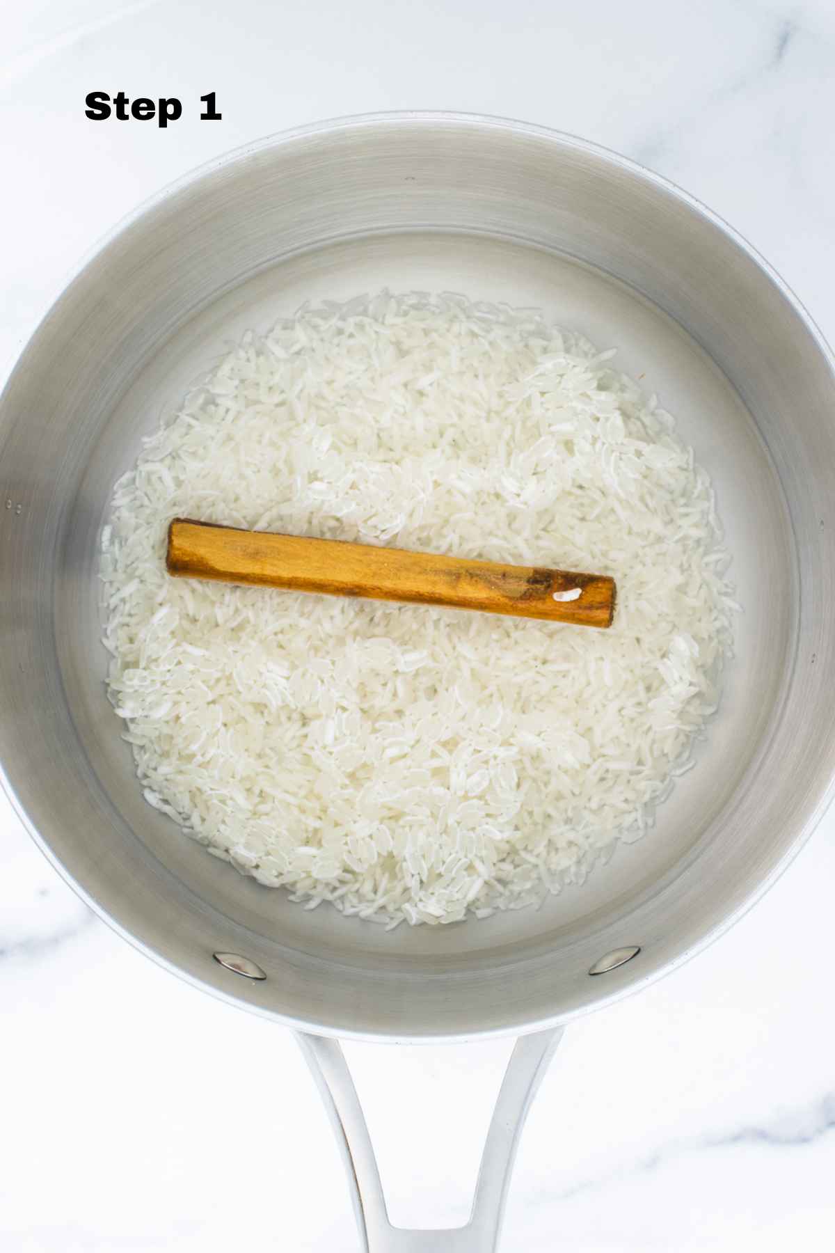 Jasmine rice in a saucepan with water and cinnamon stick.