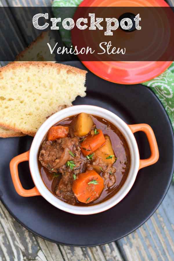 Crockpot Venison Stew in overhead shot showing meat, potatoes, and carrots in the serving dish with homemade bread to the left.