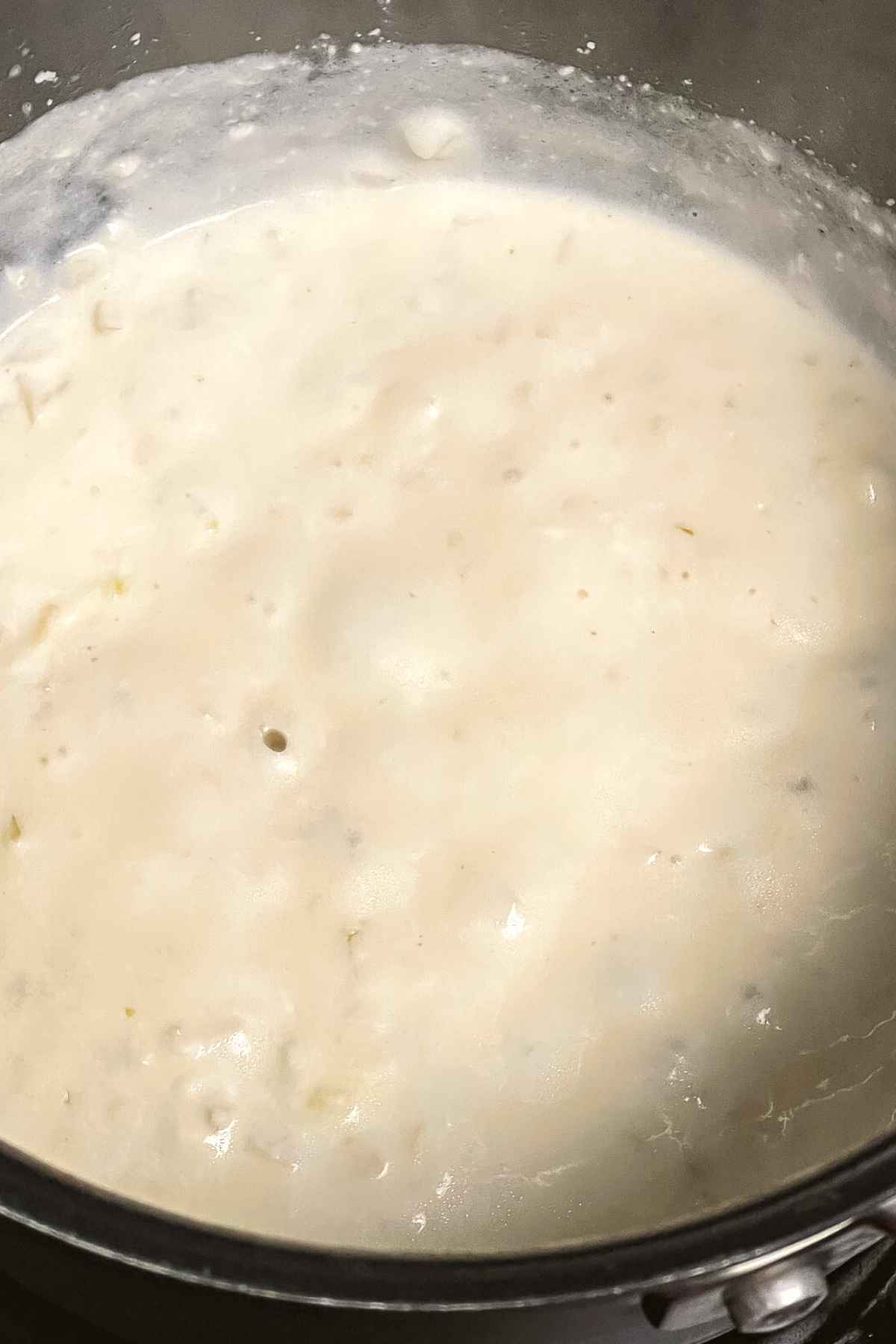 Simmering the alfredo sauce to thicken.