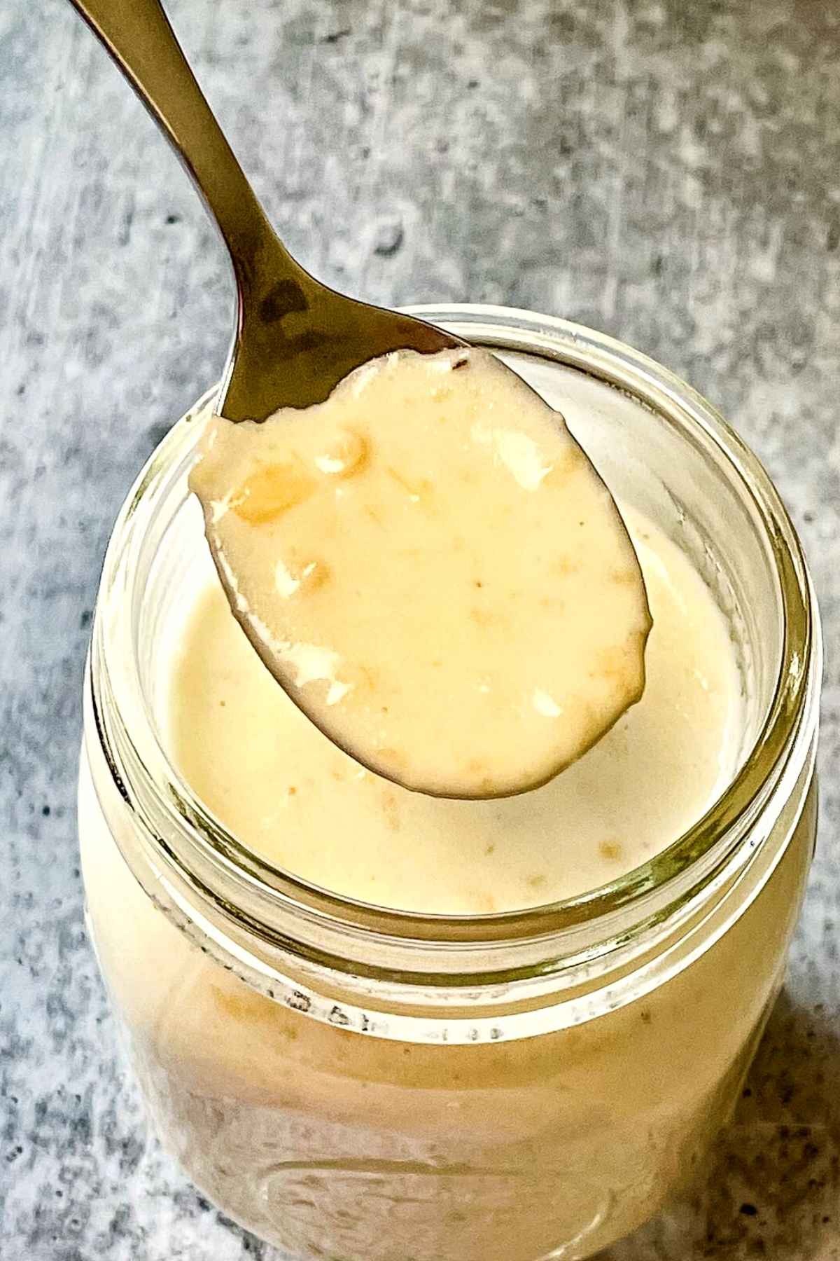 A spoon full of easy homemade alfredo sauce over top of a jar of sauce.