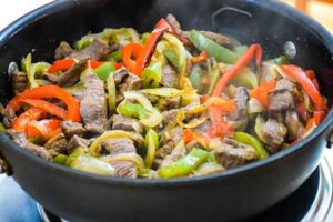 A large skillet with strips of cooked venison, peppers, and onions.