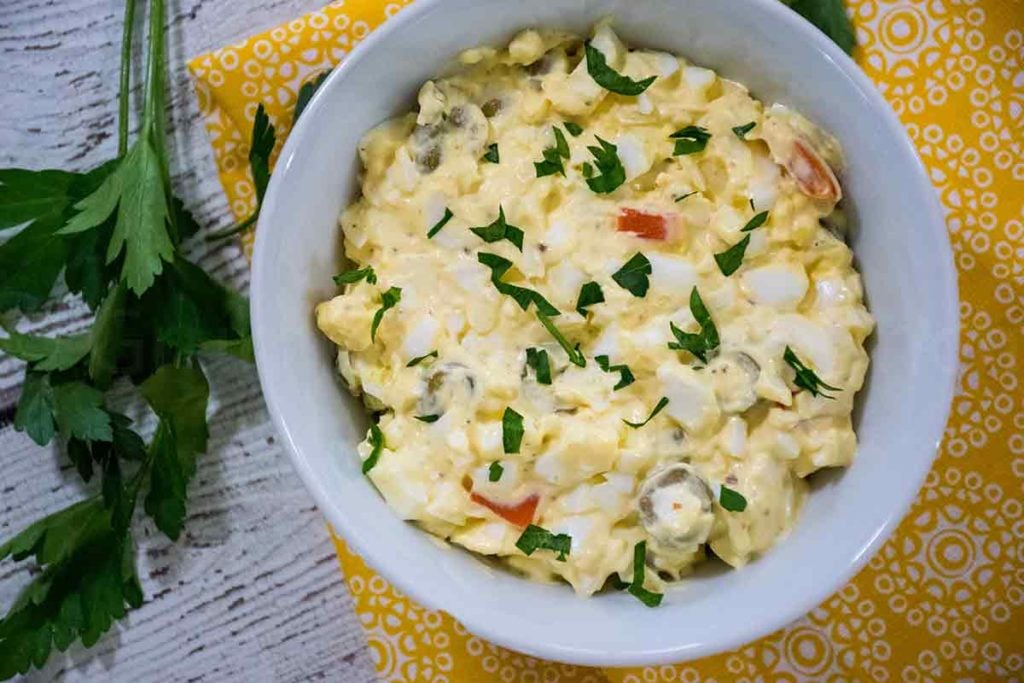 Overhead image of egg salad in a bowl with a yellow napkin and parsley sprinkled on top and to the side
