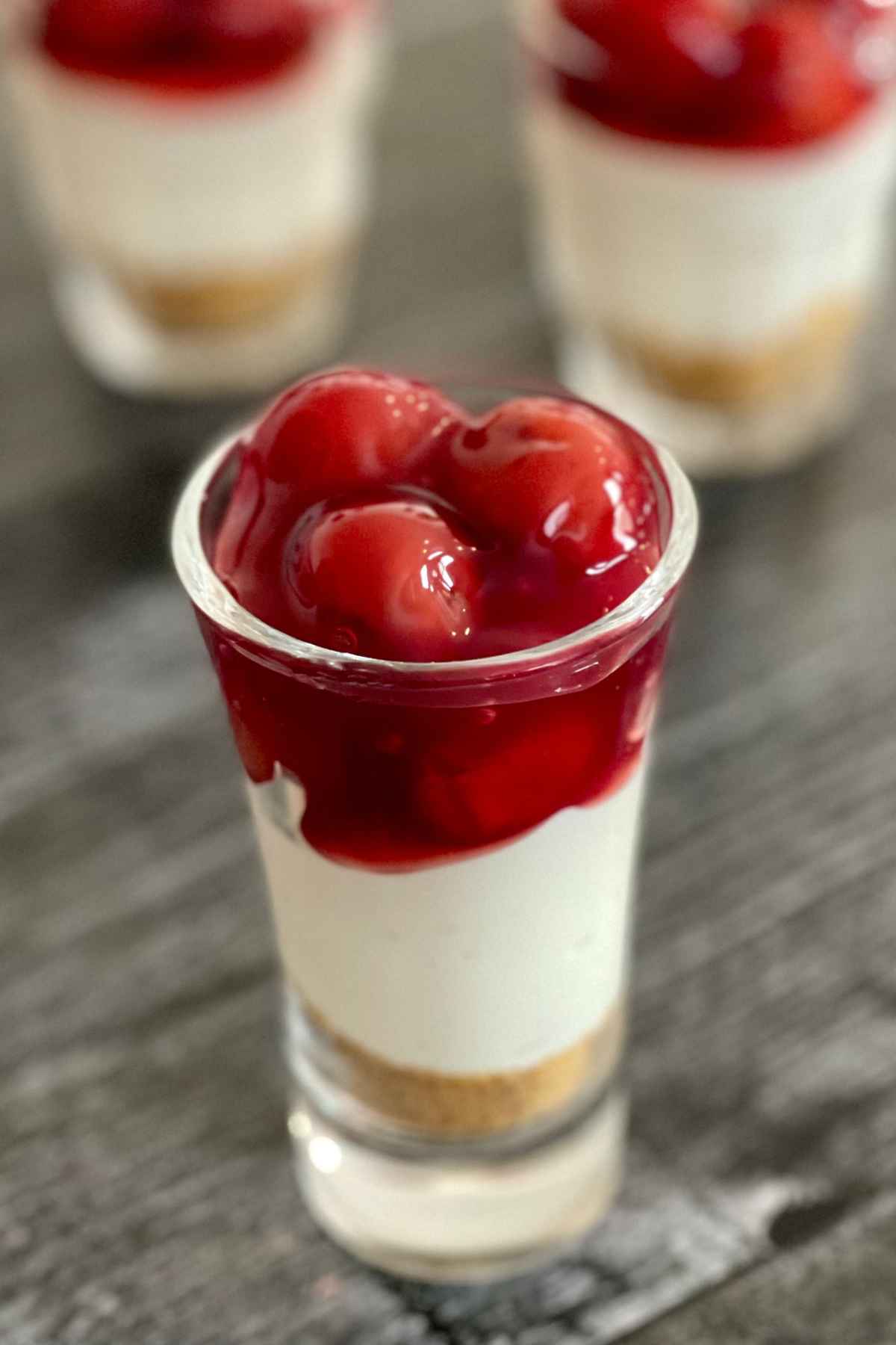 Upclose image of dessert cheesecake shooter topped with cherry pie filling.