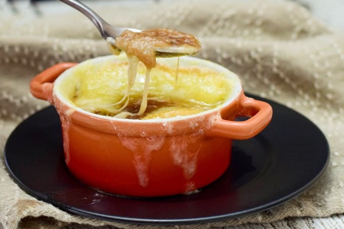 A spoon with soup and cheese stringing from the spoon to the bowl.