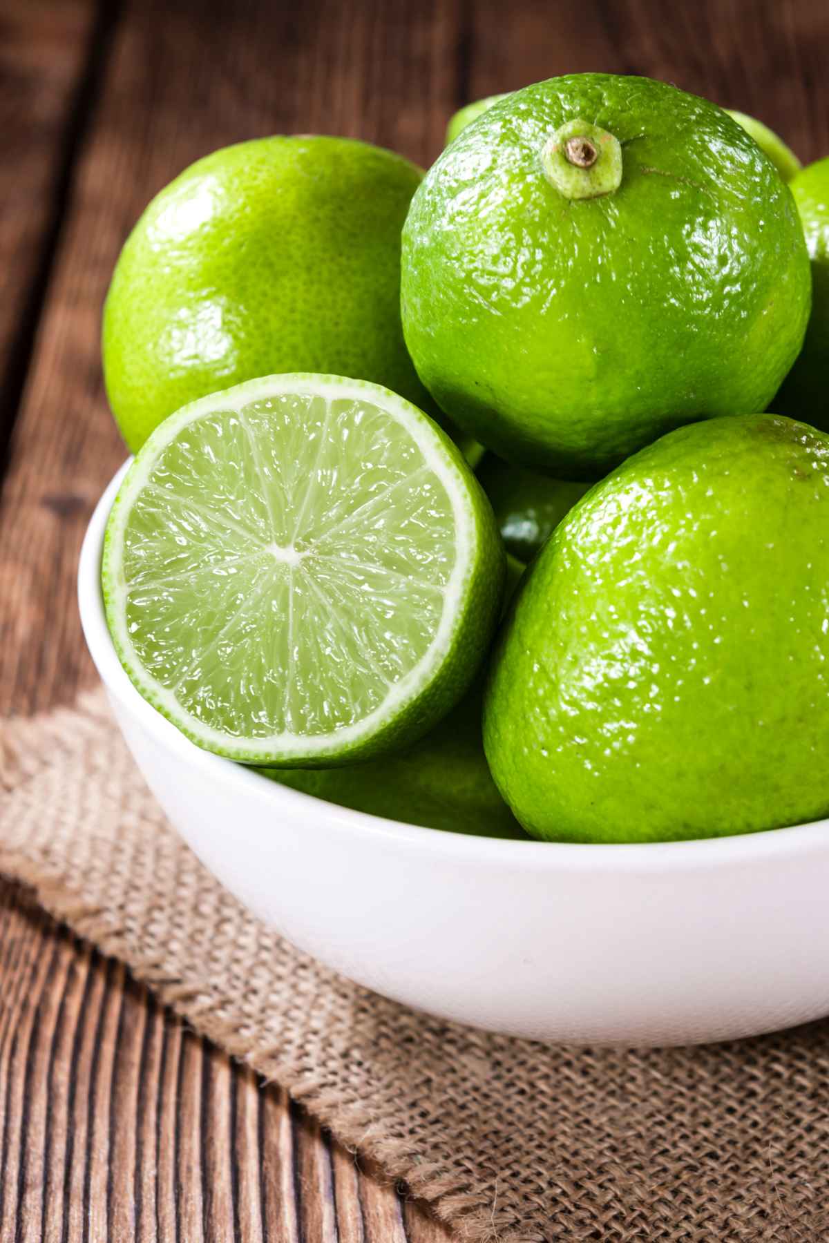 A bowl of fresh limes with one lime cut in half and facing out of the bowl.