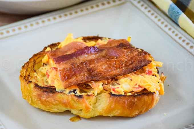 A toasted half of croissant with pimento cheese and bacon on top.