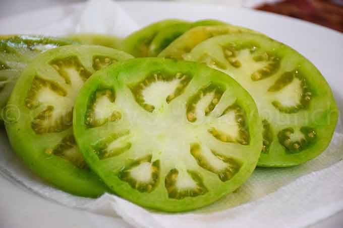 Fresh cut slices of green tomato on a white plate.