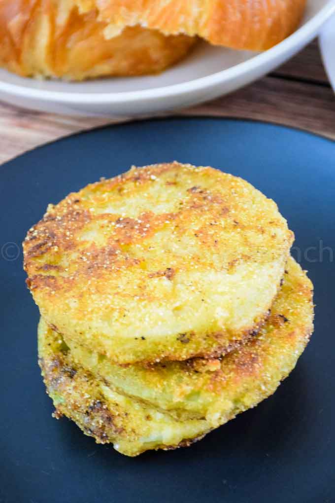 A stack of fried green tomatoes on a black plate.