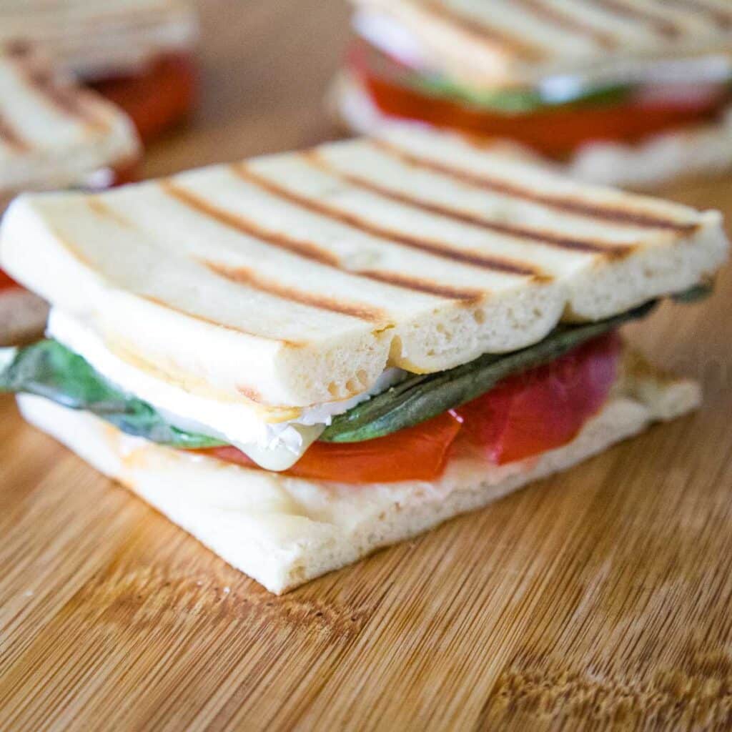 Fully assembled brie tomato sandwich with a layer of flatbread cheese, tomato, basil, and more cheese
