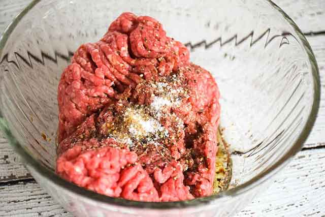 ground beef in a clear mixing bowl with seasonings on top