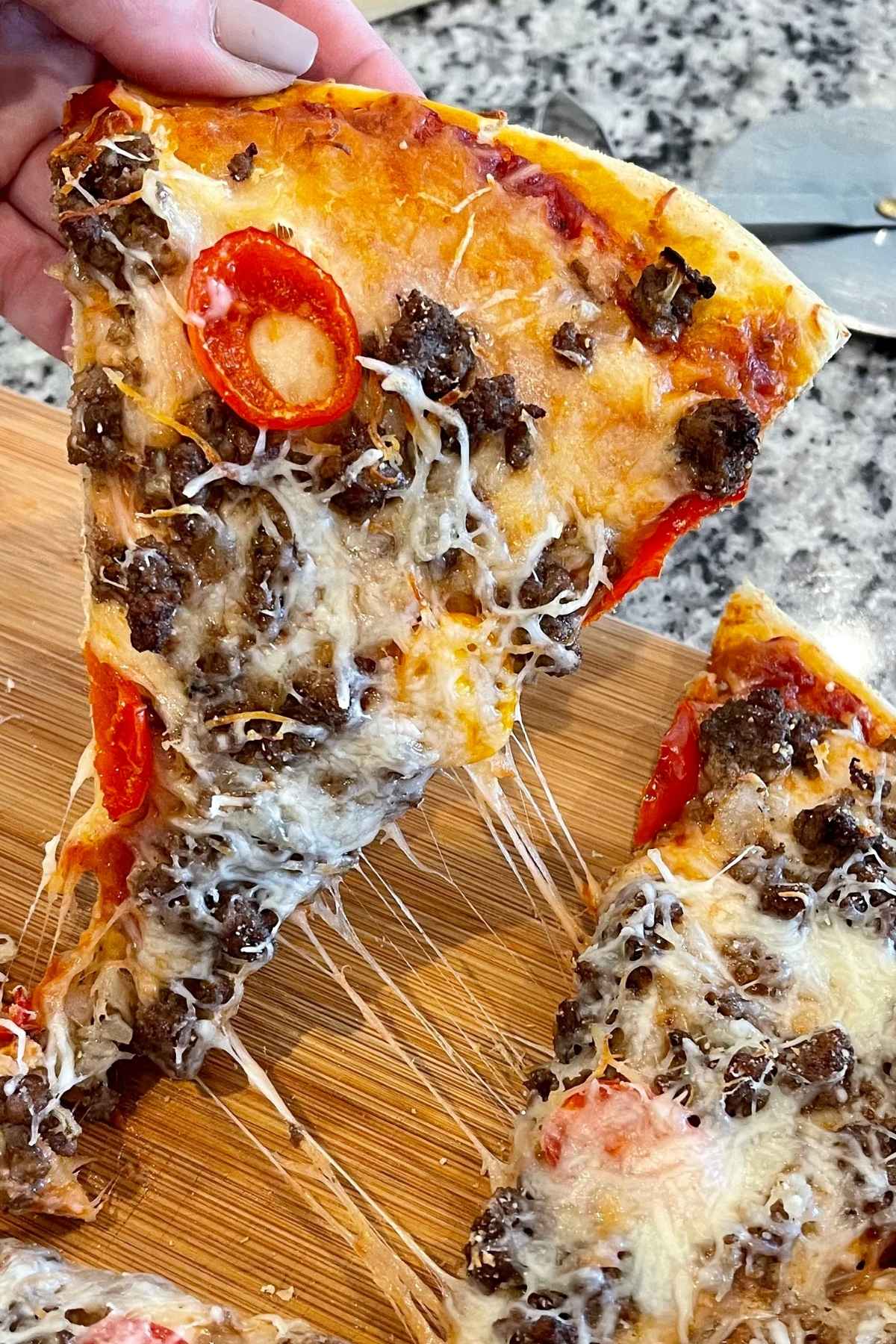 A slice of pizza being pulled away from the pie with cheese string attachments.