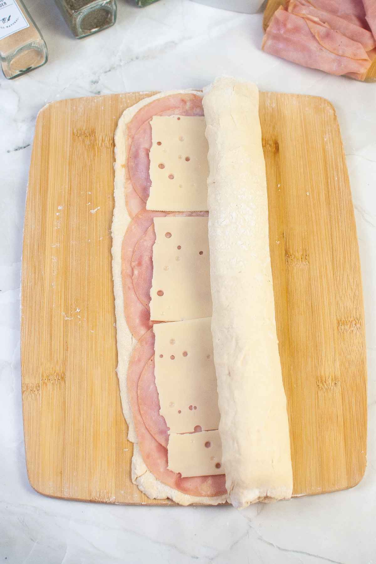 Ham and cheese on pastry being rolled up on a wood board.