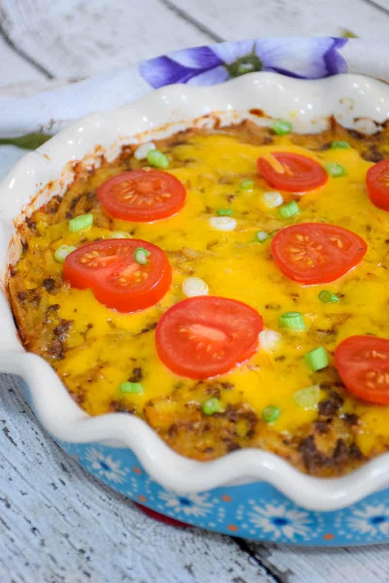 Overhead image of mexican taco casserole topped with cheese, tomatoes, and green onions.