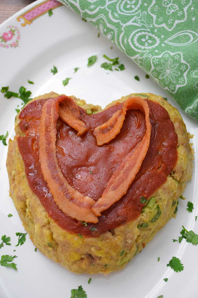Overhead image of heart shaped veal meatloaf with ketchup topping and heart shaped bacon.