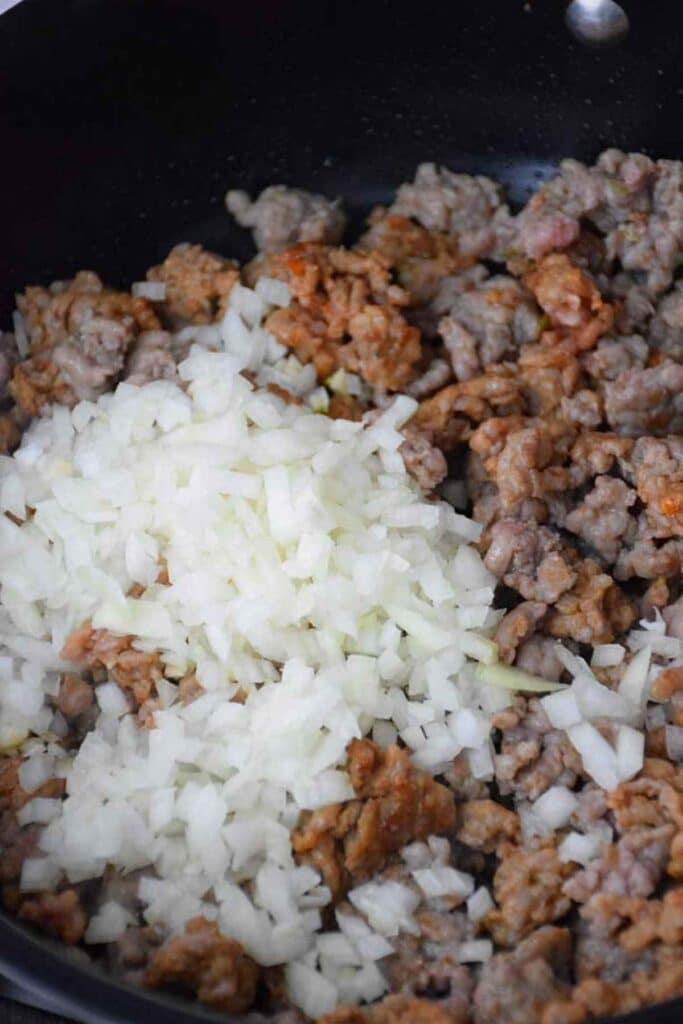 Partially cooked hot sausage with garlic and onion in a skillet.