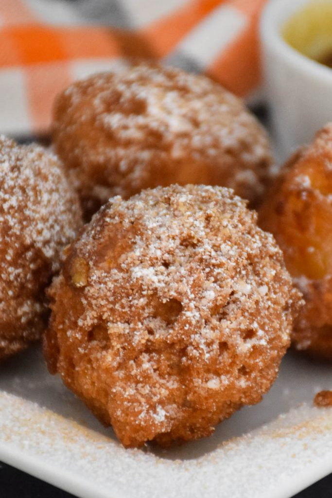 A white plate with homemade Apple Fritters donuts that are dusted with confectioner sugar sprinkled on top.
