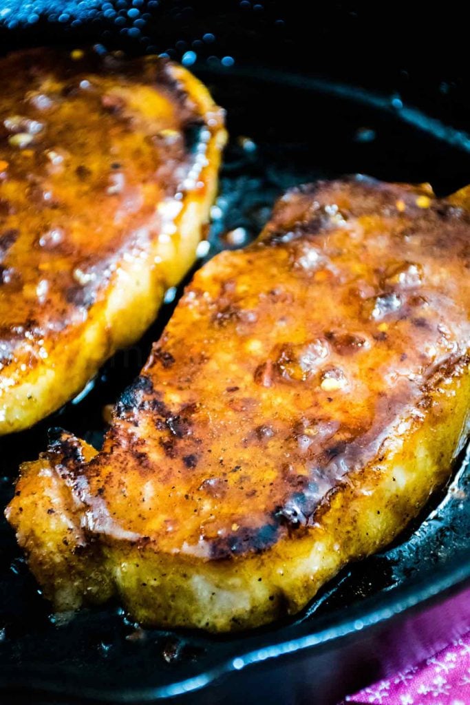 Two cooked honey garlic pork chops in a cast iron skillet.