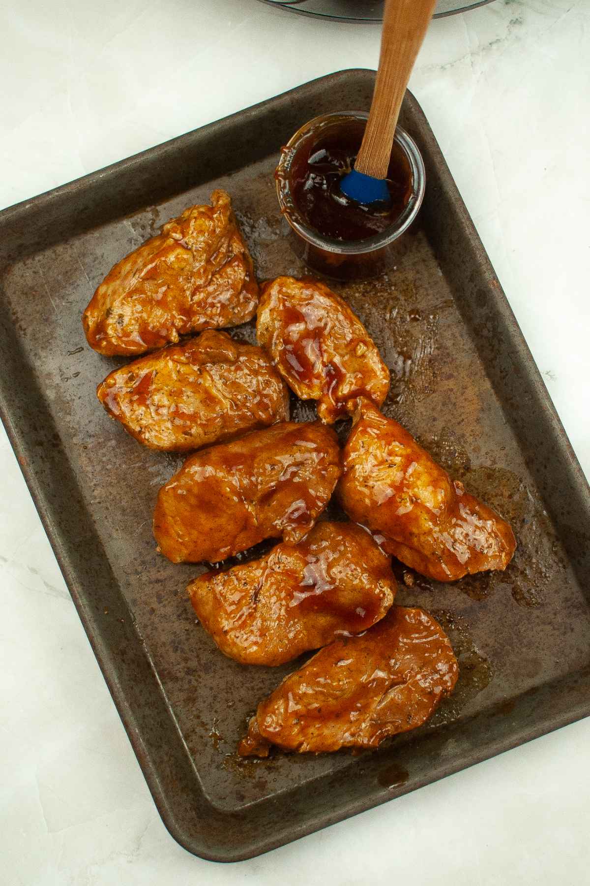 Cooked country style ribs on a baking sheet brushed with barbecue sauce.