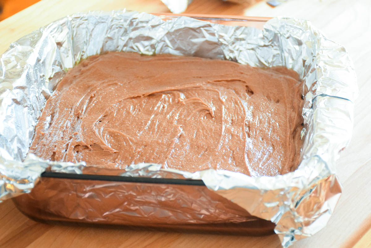 Brownie batter in a foil lined baking dish.