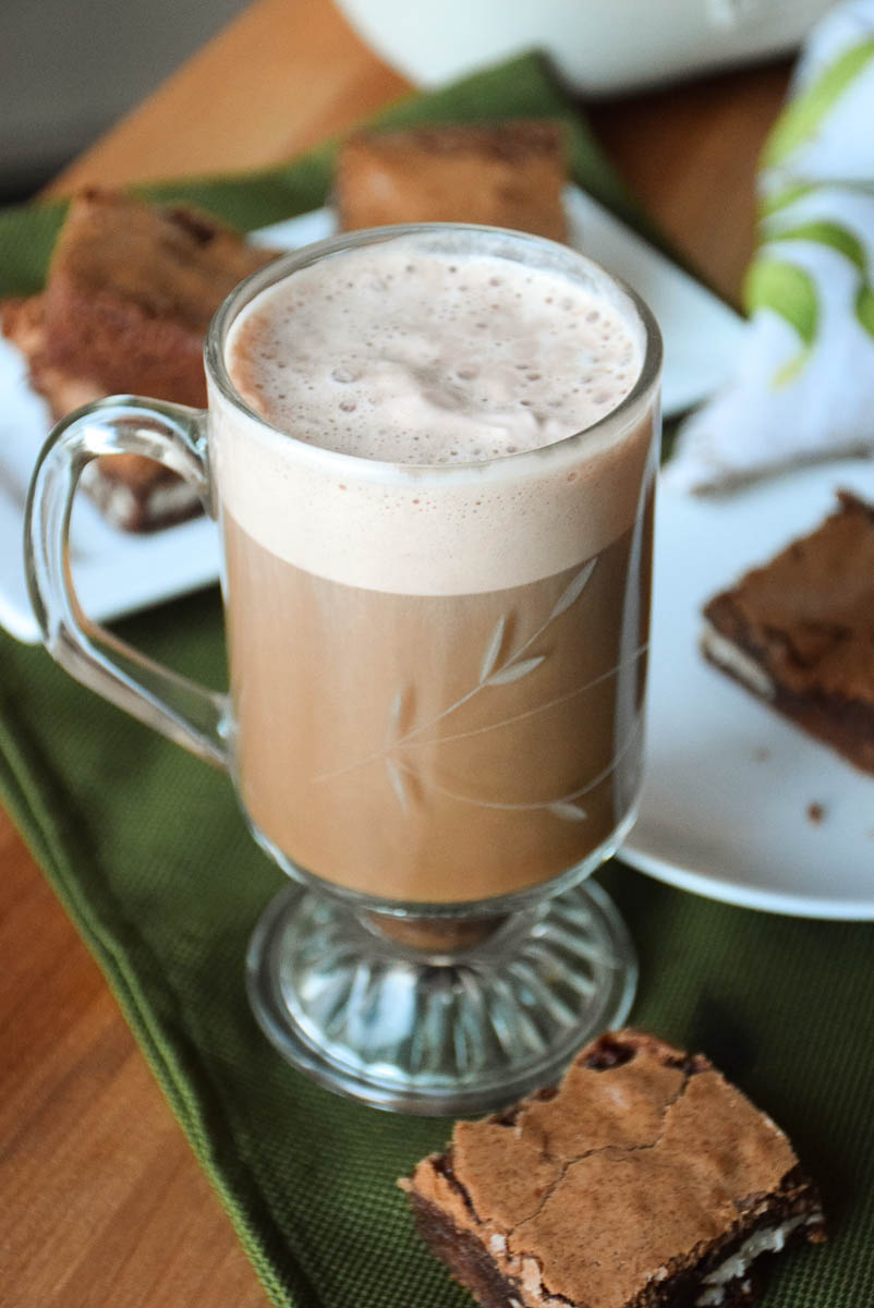 A hot latte in a glass mug with a brownie next to it on a green napkin.