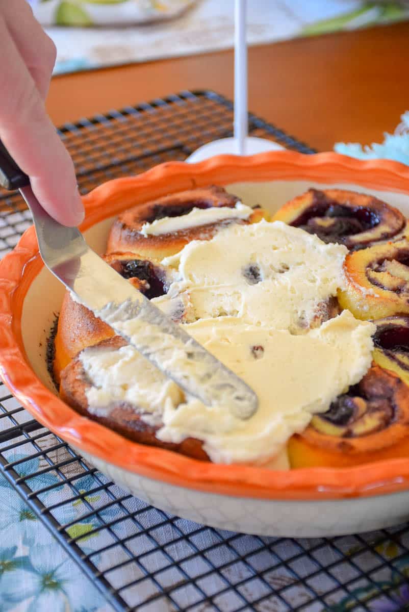 Spreading icing on the baked blueberry rolls.