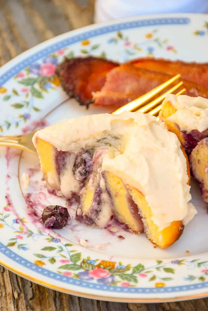 Keto Blueberry Sweet Roll that had been cut in half on a flowered plate with a side of bacon.