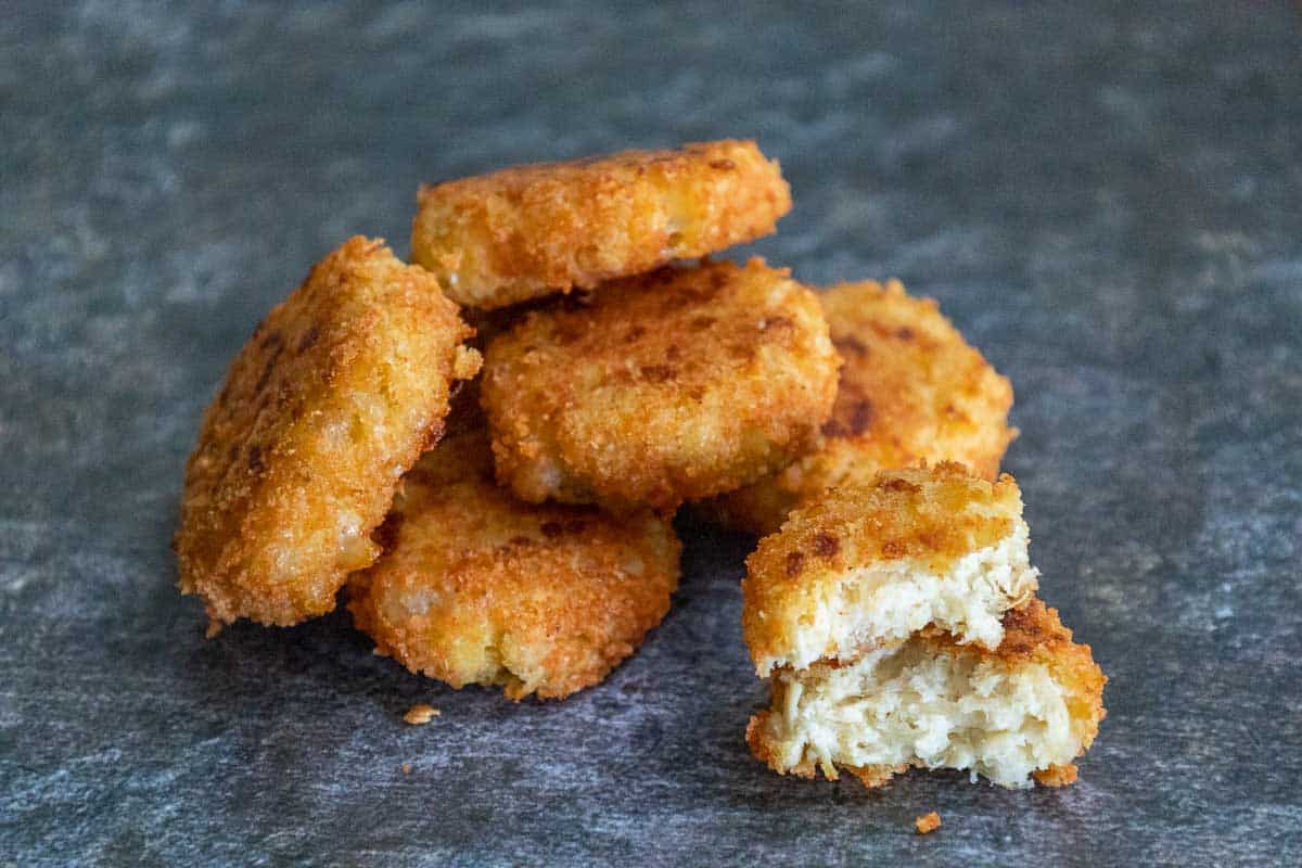 One keto chicken nugget broken in half and stacked with more whole nuggets stacked in the background.