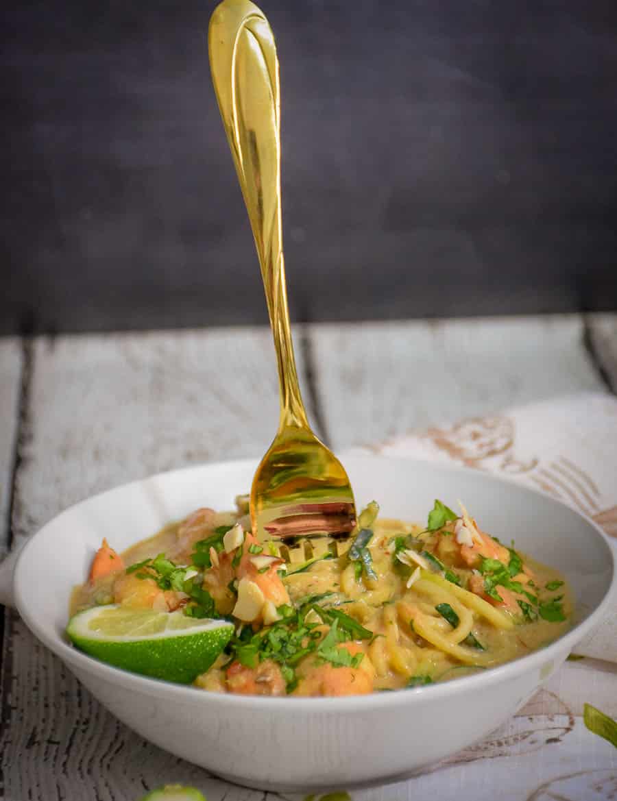 A gold fork wrapped with zucchini noodles standing up in a bowl.