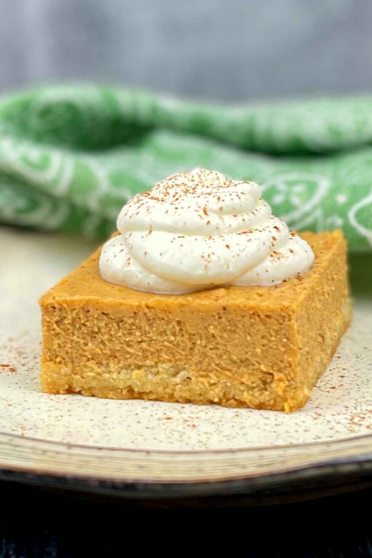 One slice of pumpkin cheesecake on a plate topped with whipped cream.