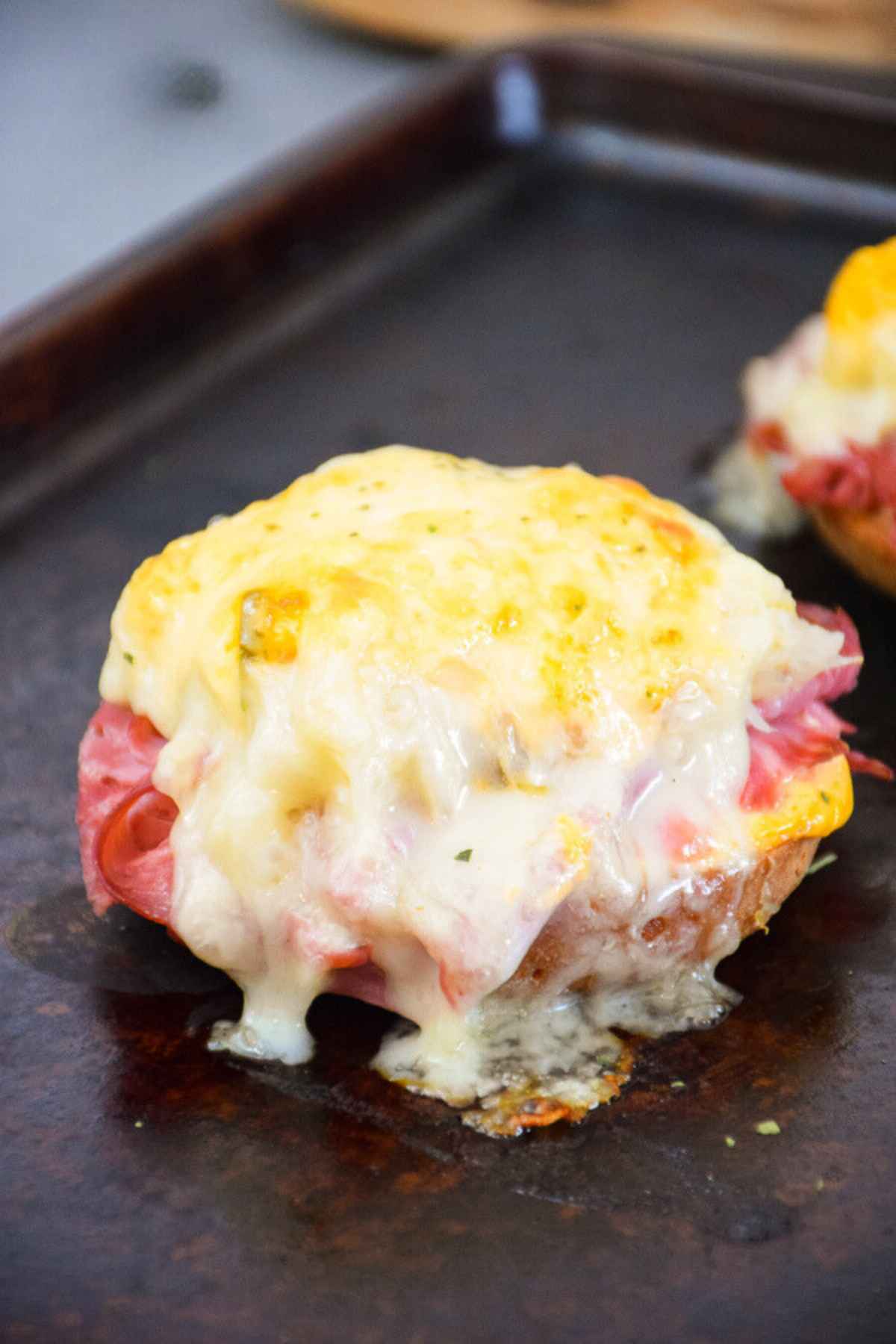 Broiled sandwich on a baking sheet with melty swiss cheese drips.