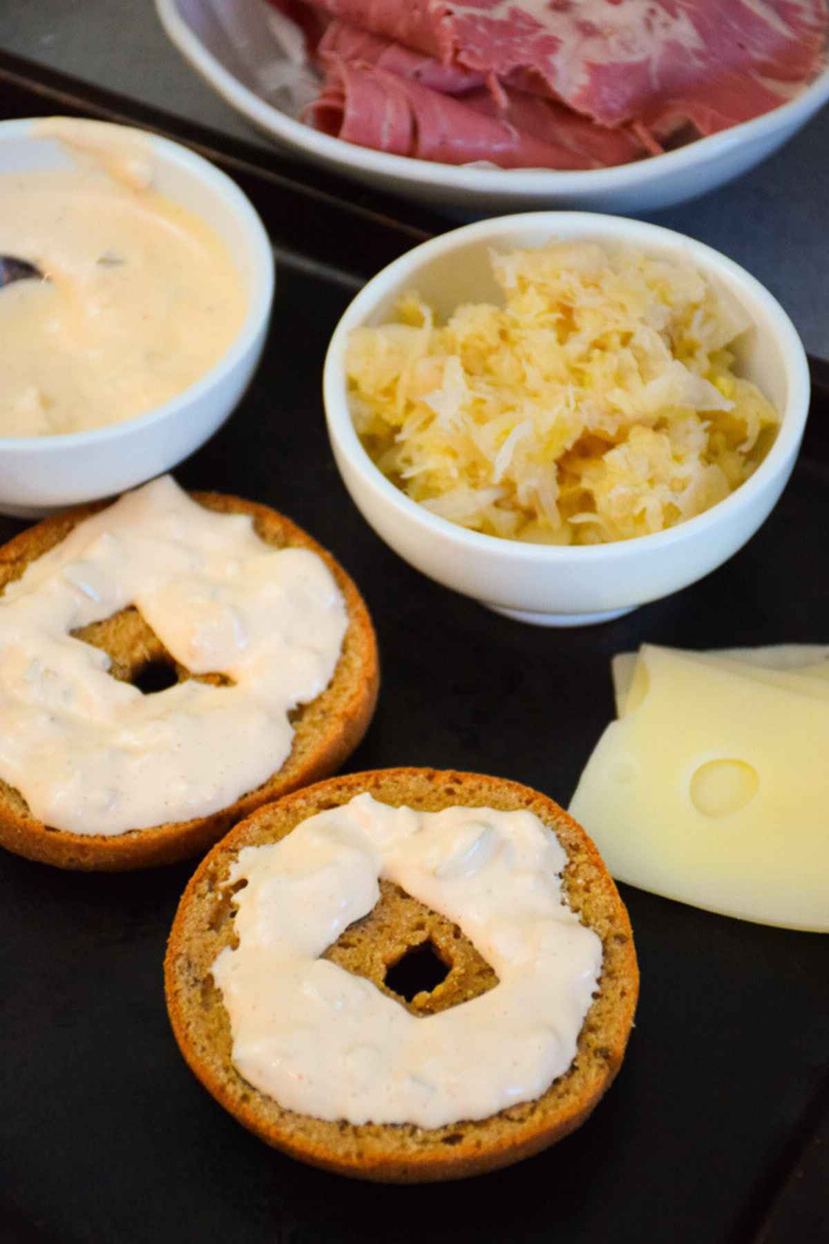 Keto rye bagel spread with sugar free thousand island dressing, and a side of swiss cheese, sauerkraut, and corned beef.