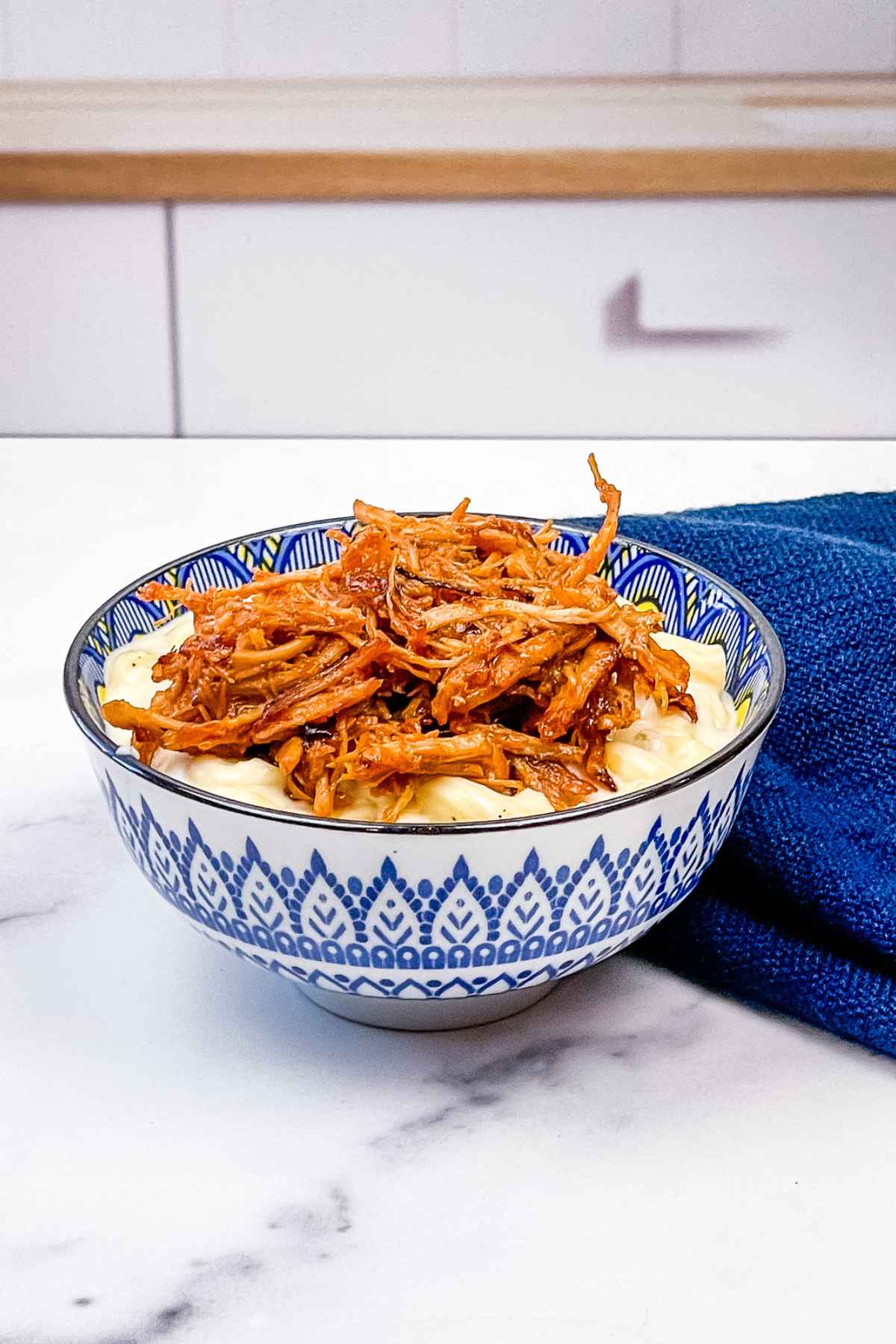 Pulled pork on top of a bowl of macaroni and cheese in a blue bowl.