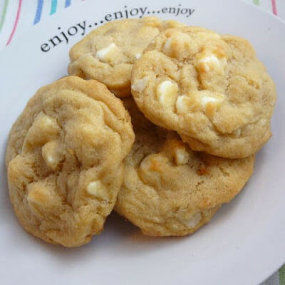 A white plate with a pile of white chocolate macadamia nut cookies on top.