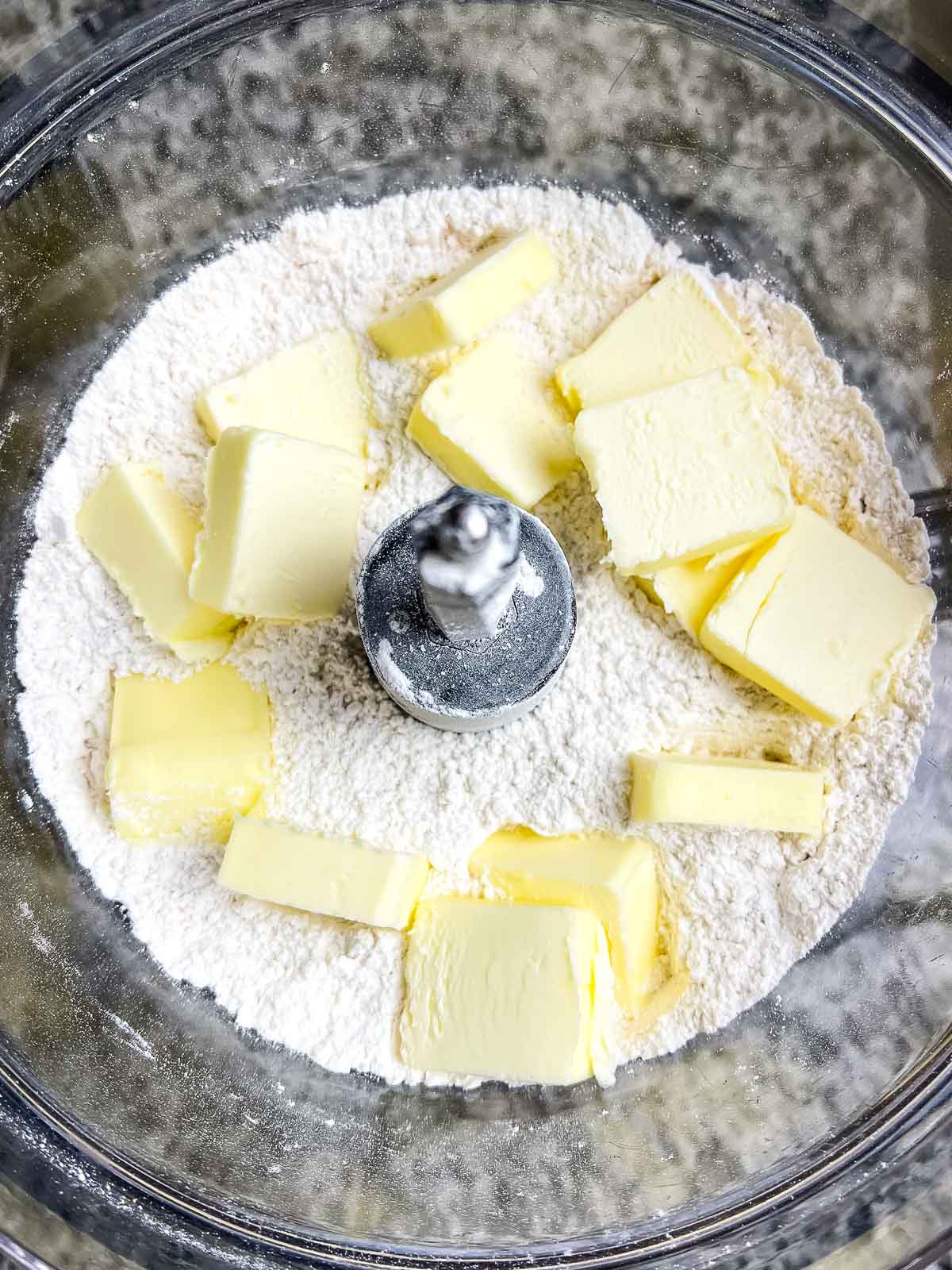 Butter pats on top of flour mixture in food processor.