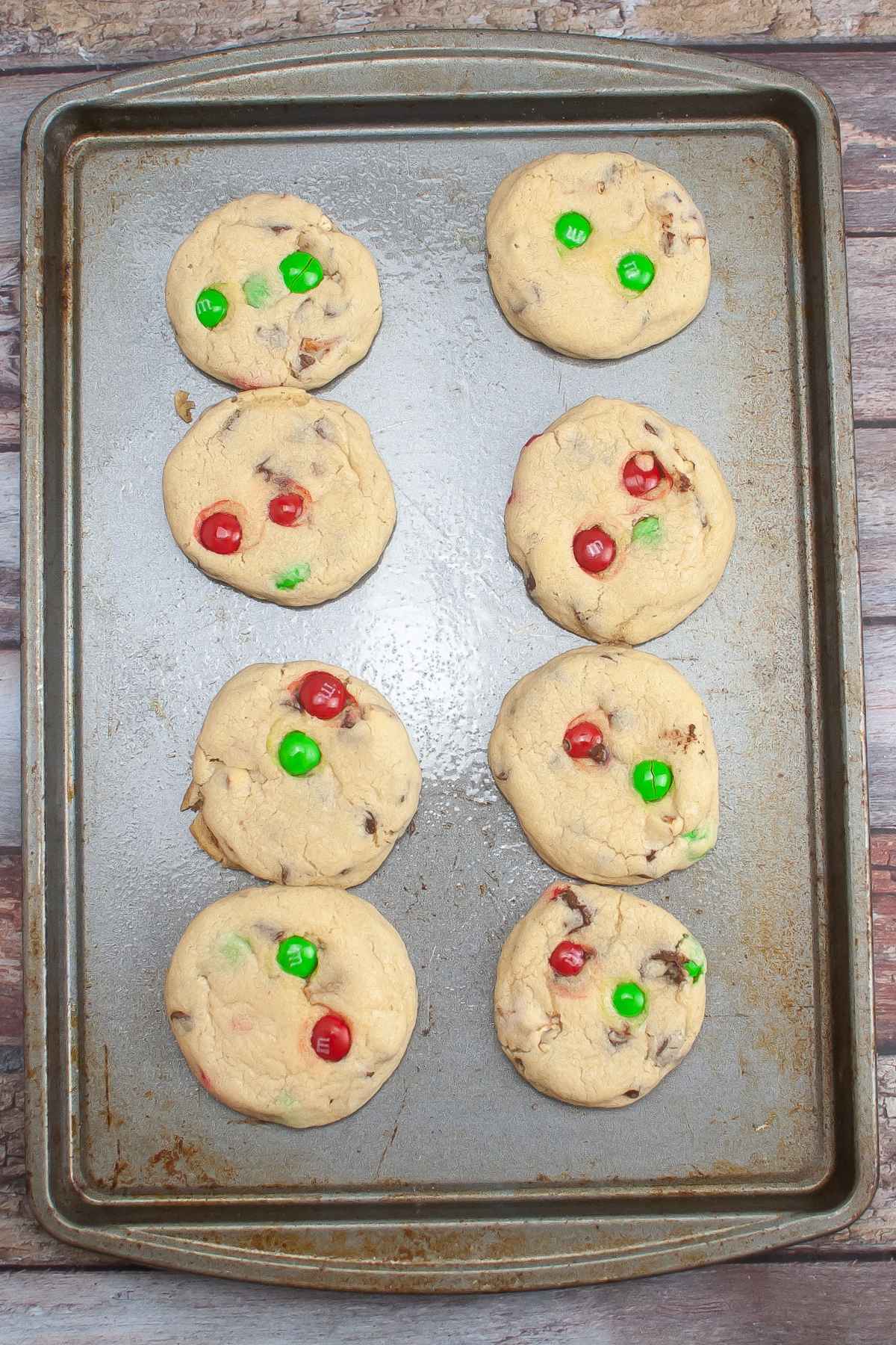 Eight baked M&M Pretzel Cookies on a baking sheet.