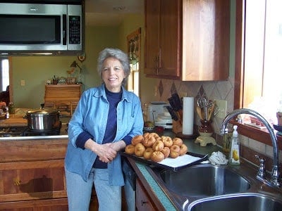 Mom standing in her kitchen with a tray of homemade buttermilk doughnuts on the counter beside her.