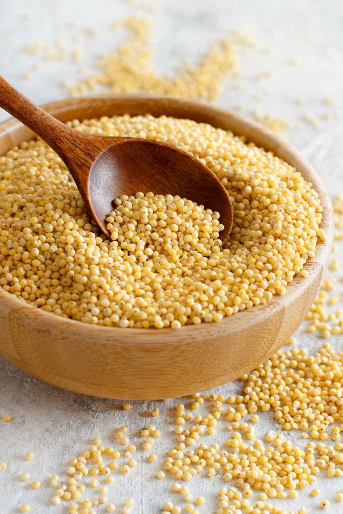 Raw millet in a wooden bowl with a wooden spoon.