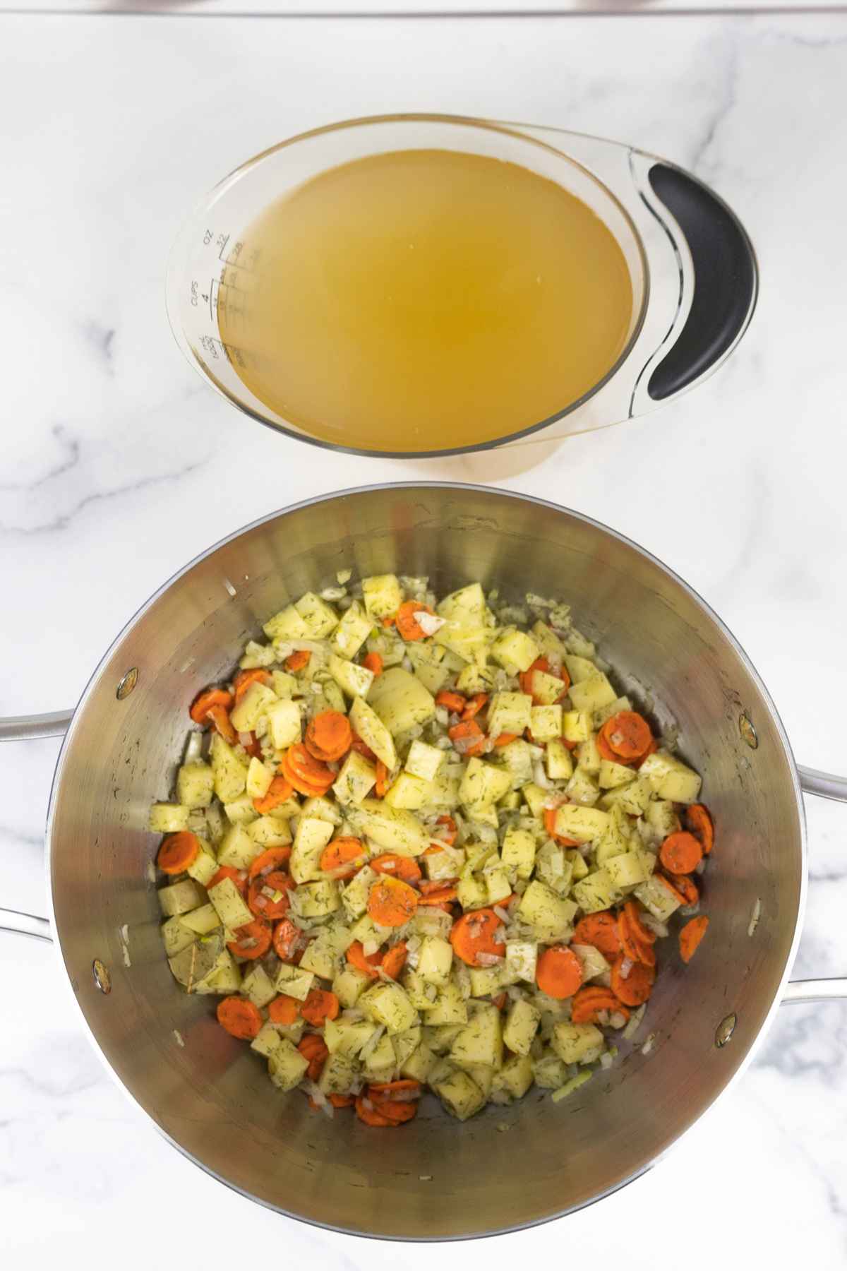 Sauteed vegetables in a soup pot with a measuring cup full of broth.