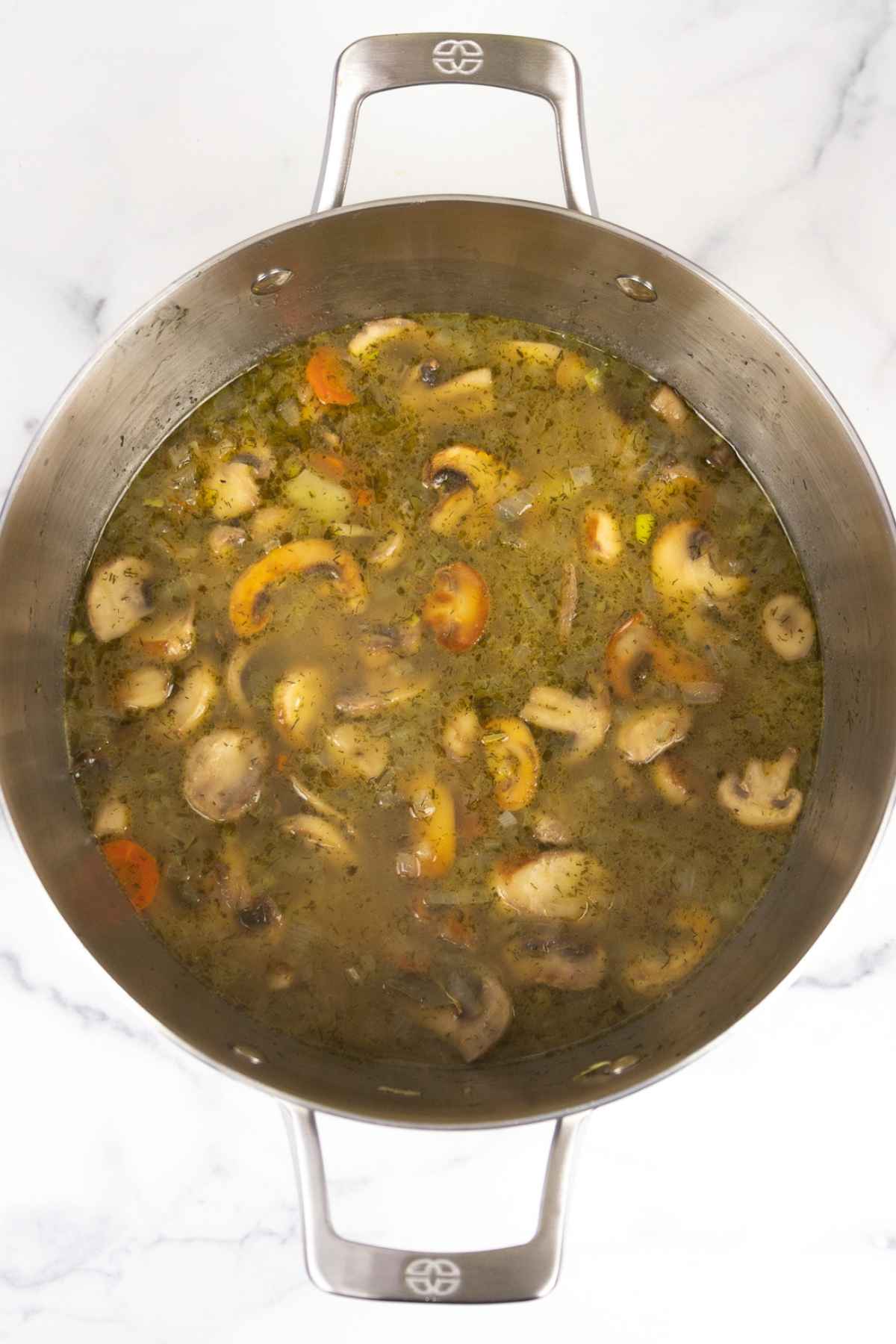 Cooked vegetables in broth in a soup pot.