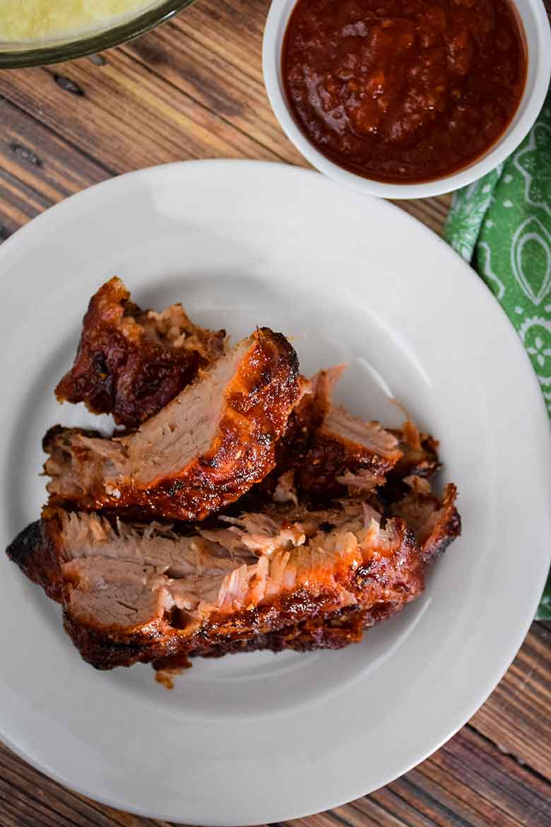 Overhead view of cooked pork back ribs with sugar-free Raspberry Chipotle Sauce on the ribs and in a dish on the side