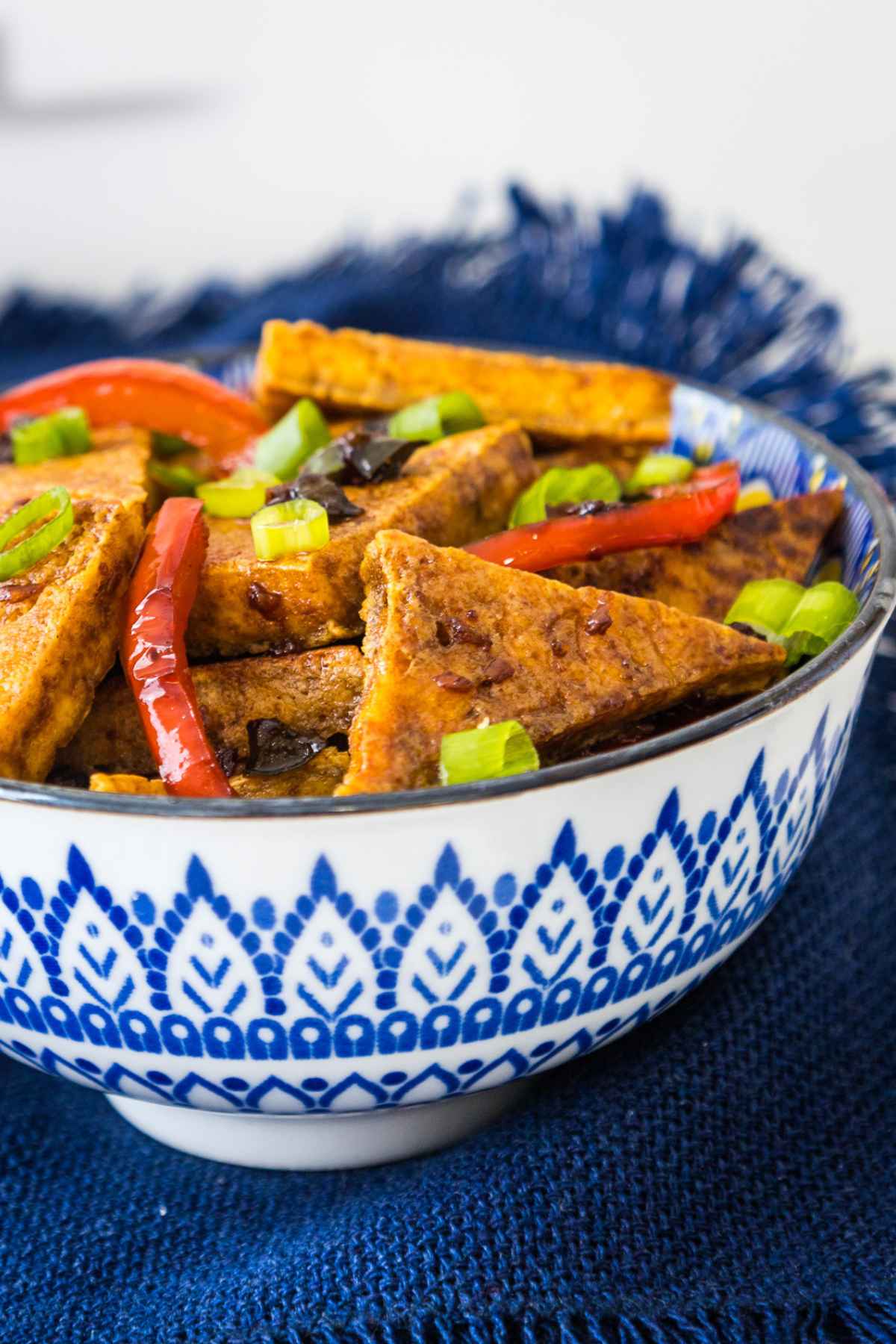 Up close images of pan fried tofu in a dark sweet and spicy soy sauce with red peppers and jalapenos.