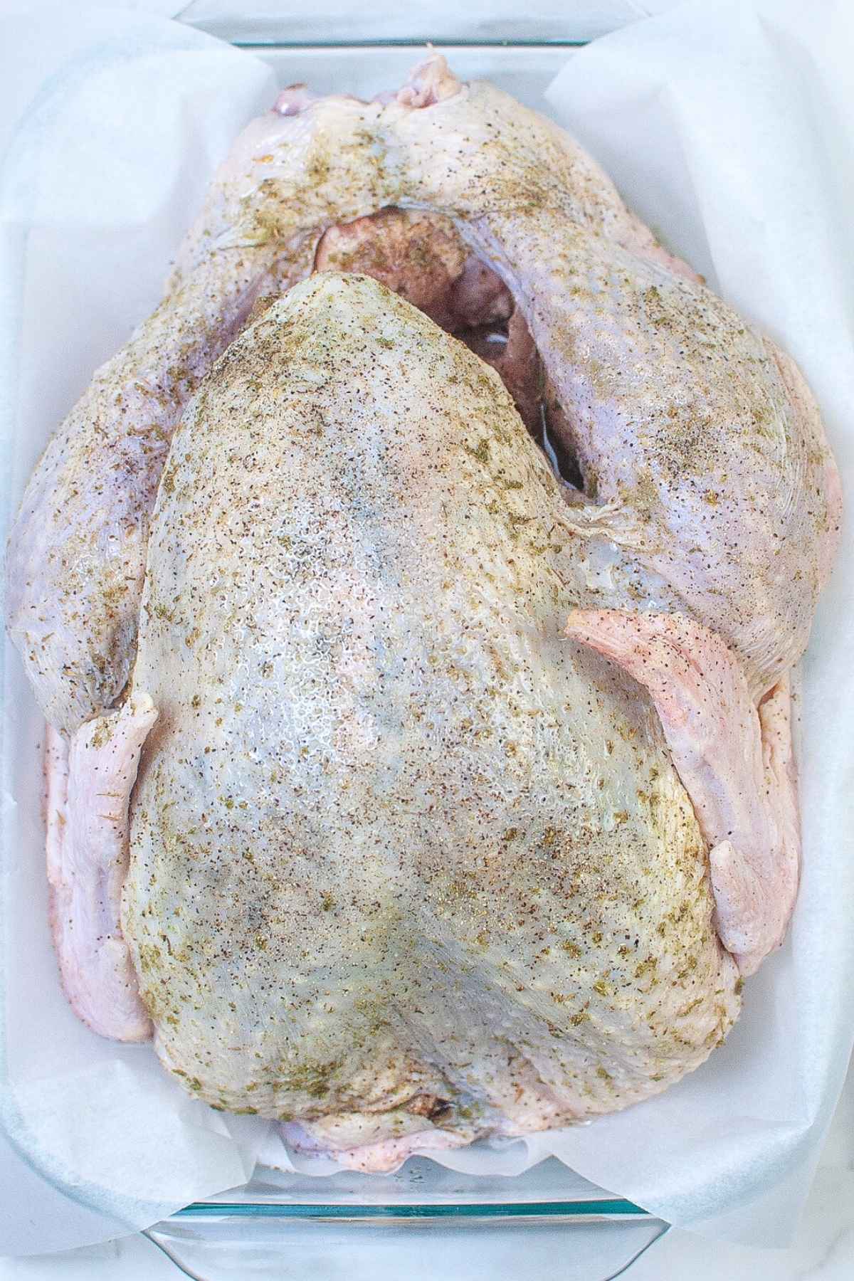 Seasoned raw whole turkey on top of parchment paper.