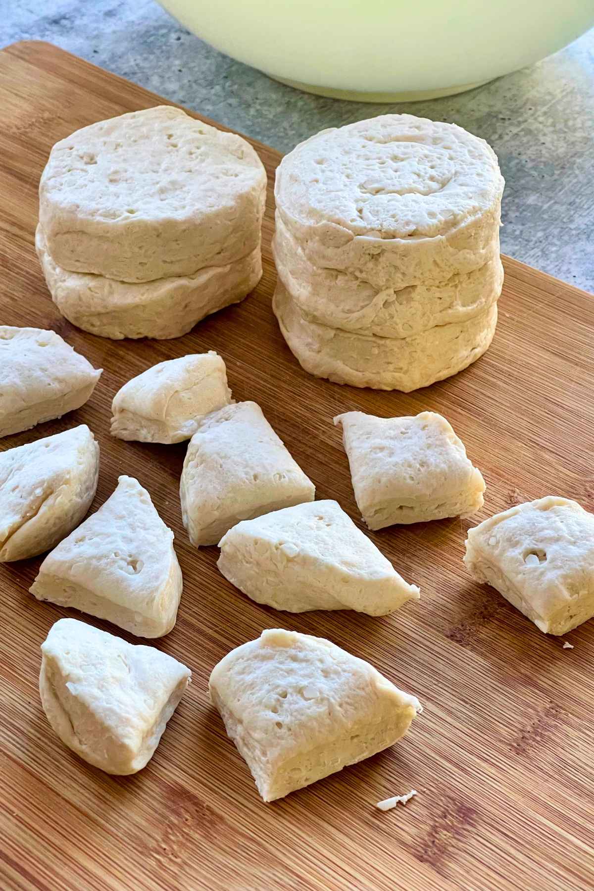 Canned biscuit dough on a wood board with some biscuits cut into quarters.