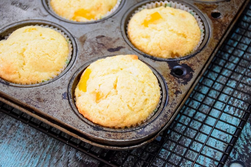 Baked Peach muffins in the muffin tin cooling on a wire rack.