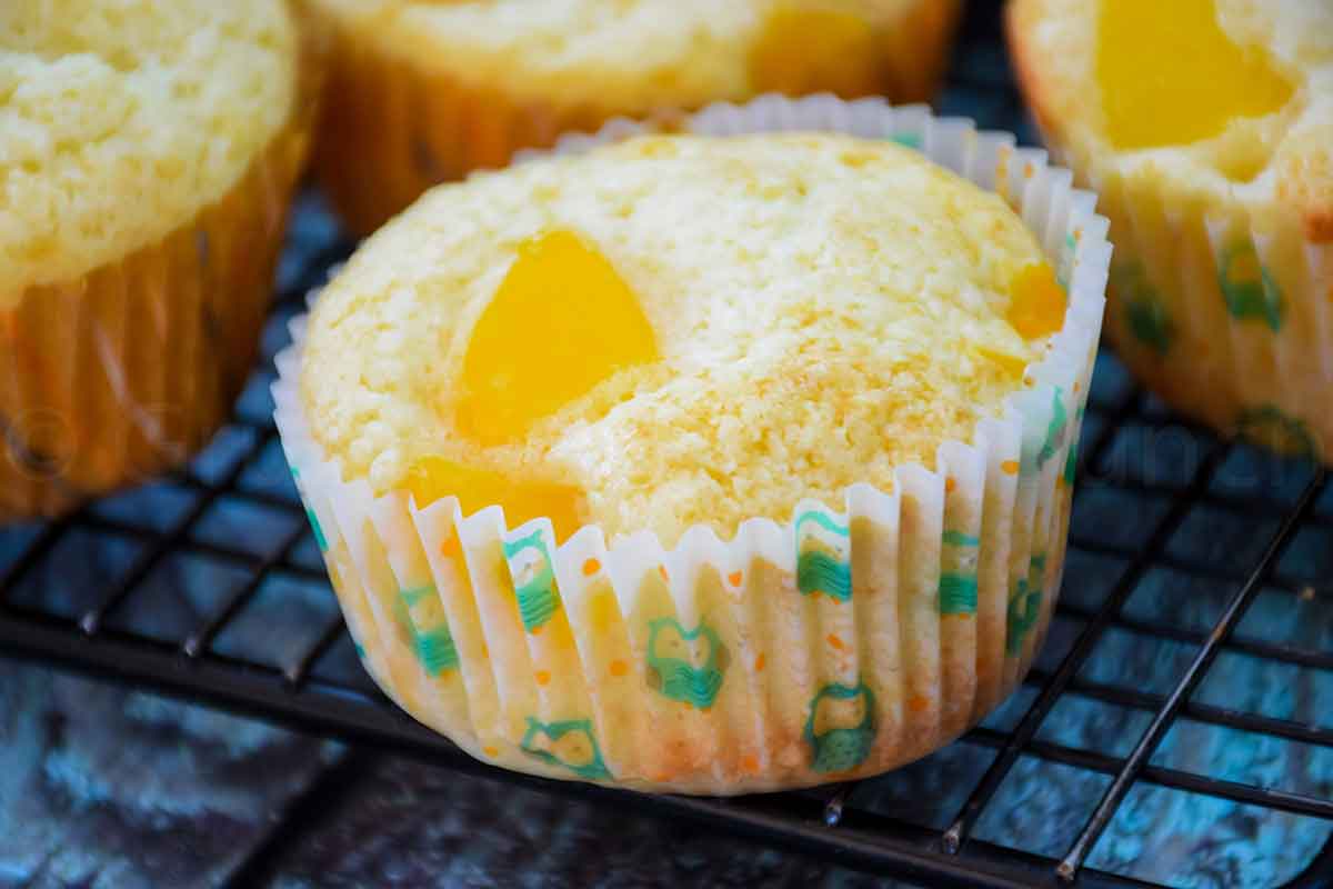 Peach Muffins on a cooling rack wrapped with a paper liner and more muffins in the background.