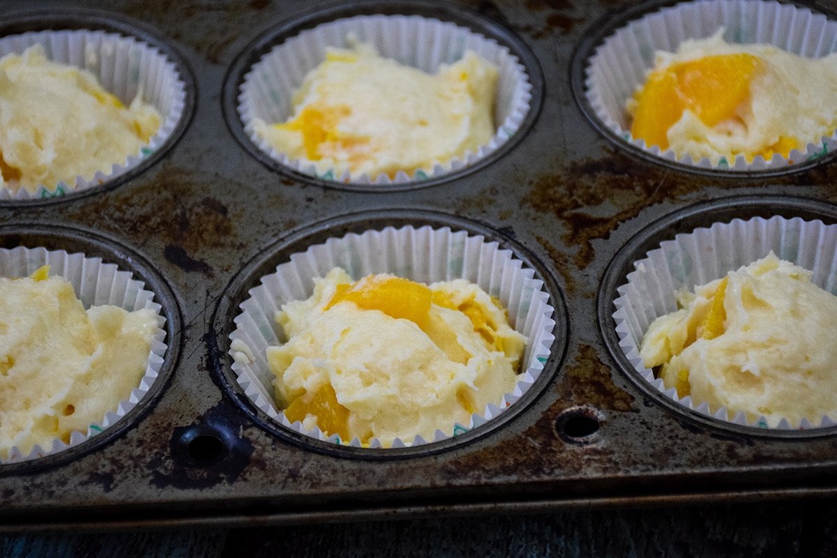 Muffin papers full of batter in a muffin pan.