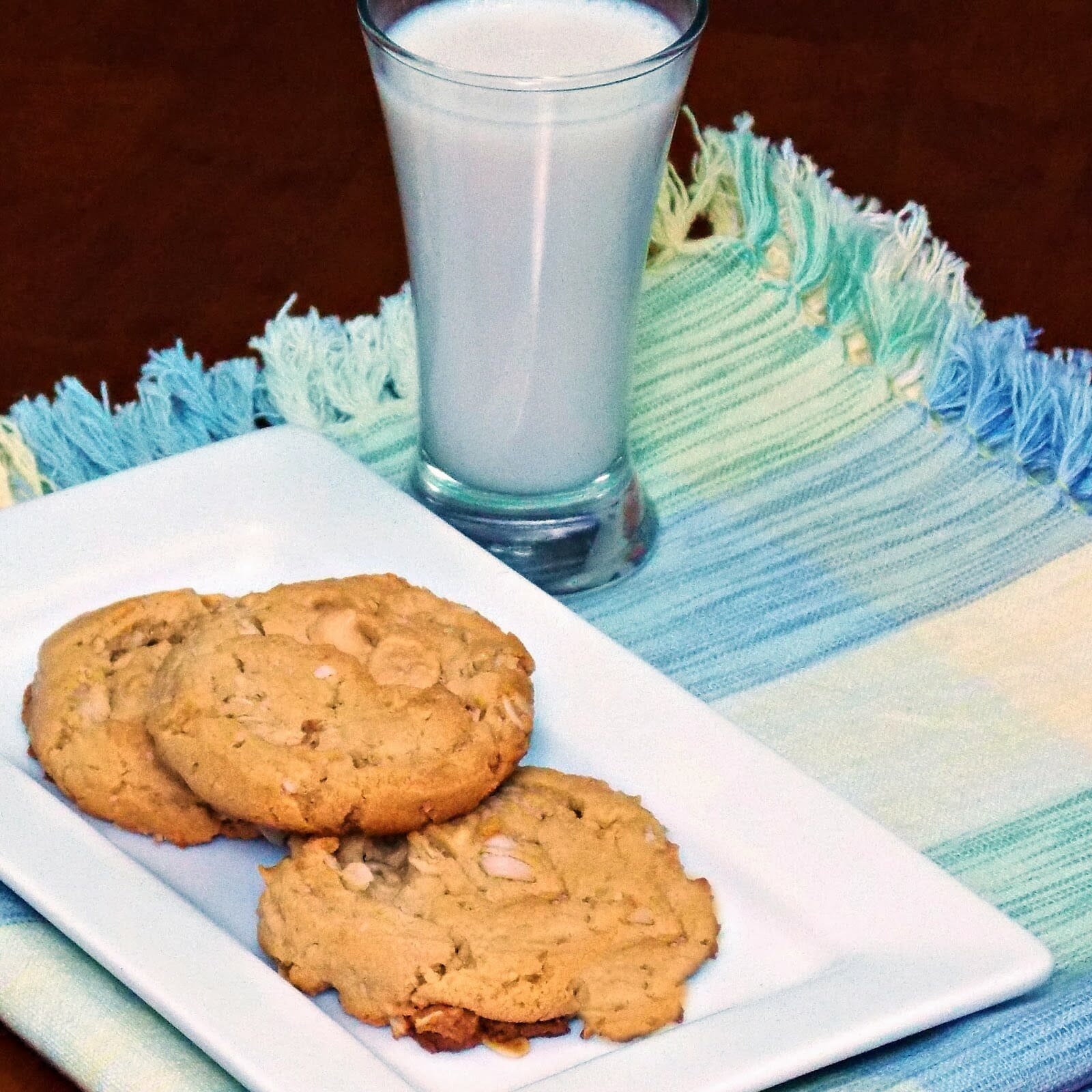 Three cookies on a white plate with a glass of milk to the right of the plate.